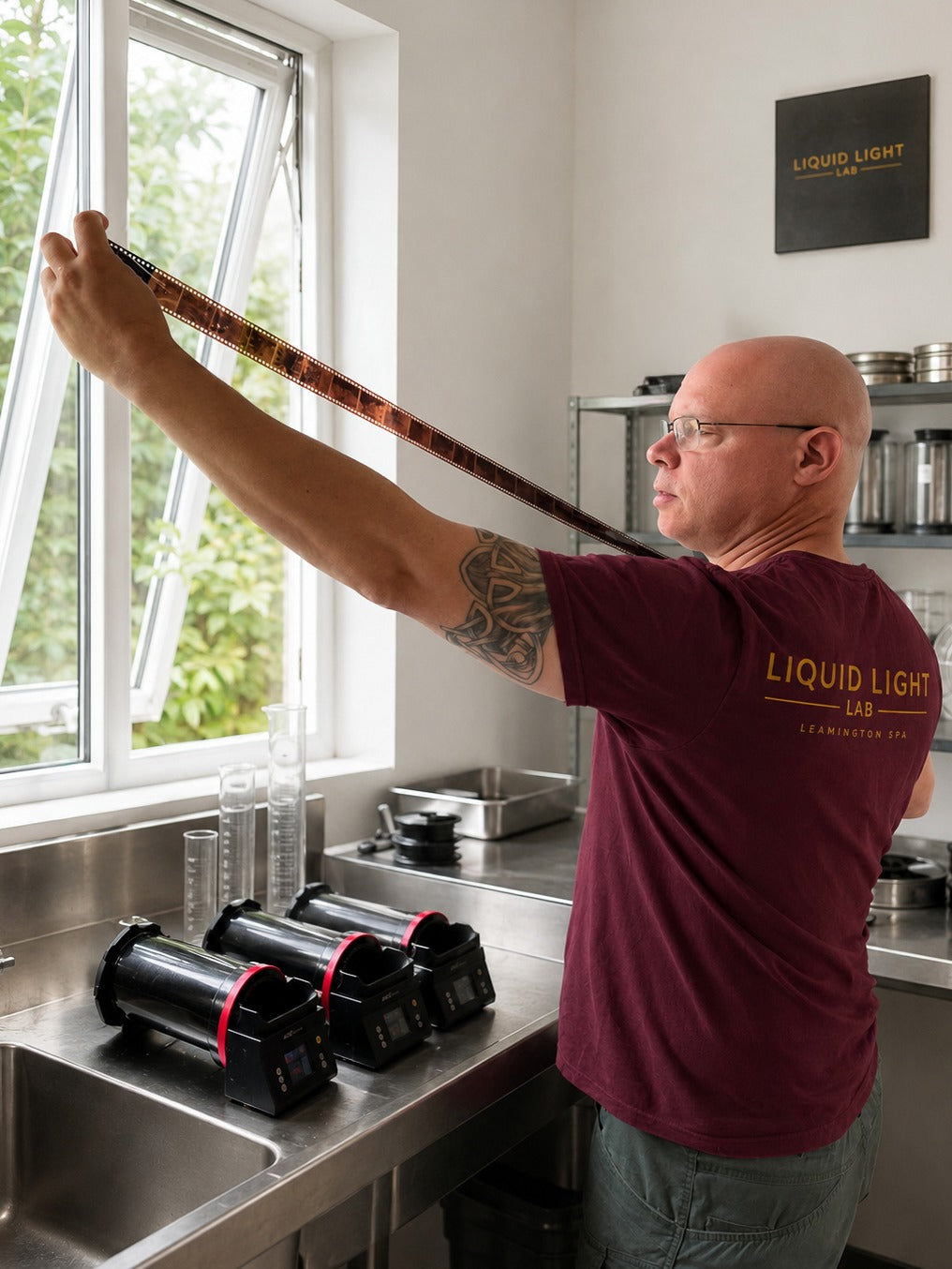 A technician at Liquid Light Lab checks a developed film strip, with three AGO Film Processors on the sink