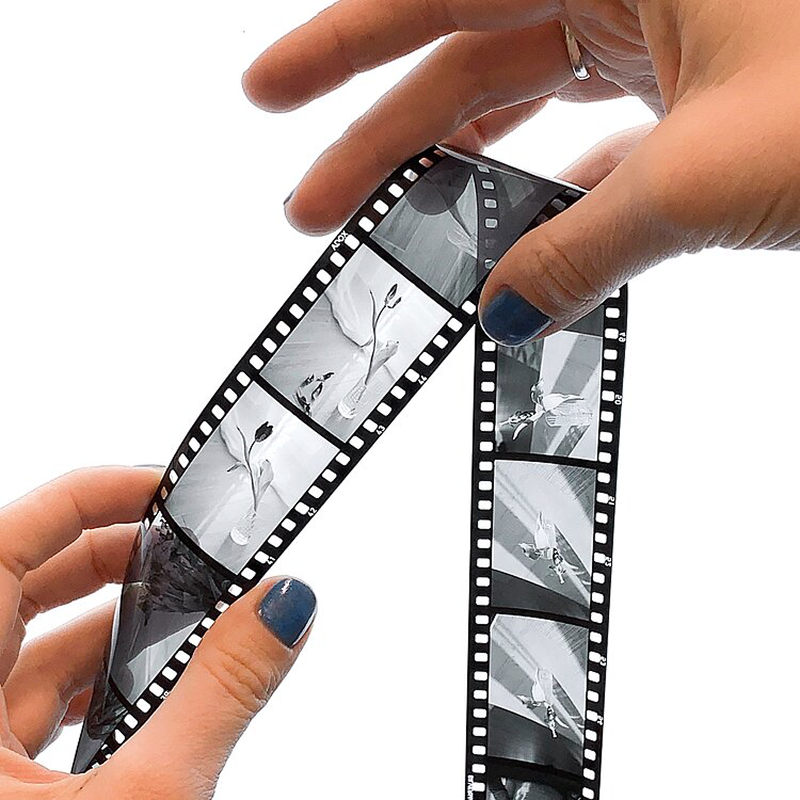 Hands holding two developed B&W reversal slide film strips examining positive transparency frames from ADOX Scala processing
