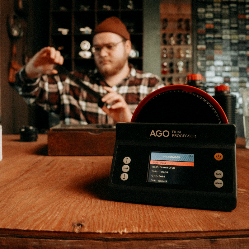AGO Film Processor showing its black and white program list on a workbench, a photographer loading film behind it