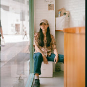 Woman sitting on a box in a room with a tiled wall and wooden furniture shot with Reflex Lab Pro 100 film 