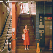 Woman in an orange dress standing on a staircase in a subway station shot with Reflex Lab Pro 100 film 