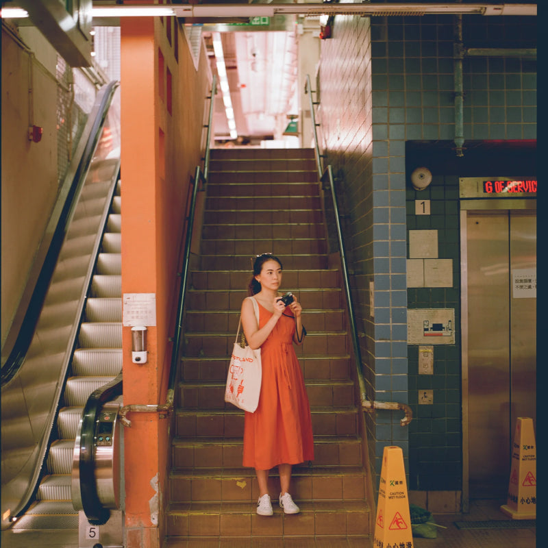 Woman in an orange dress standing on a staircase in a subway station shot with Reflex Lab Pro 100 film 