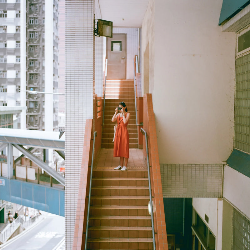 Woman in an orange dress standing on a staircase in an urban setting shot with Reflex Lab Pro 100 film 