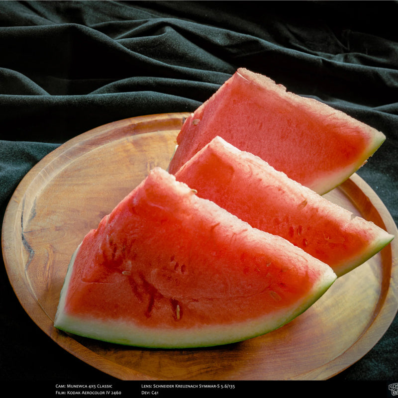 Three slices of watermelon on a wooden plate with a dark background shot with Pro100 4x5 sheet film